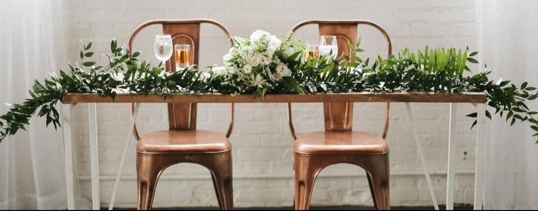Wedding reception sweetheart table with industrial chairs and a greenery runner.